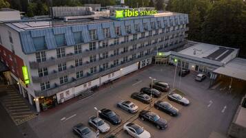 Un edificio de varios pisos con estacionamiento, un letrero que dice 'ibis styles' y una entrada visible.