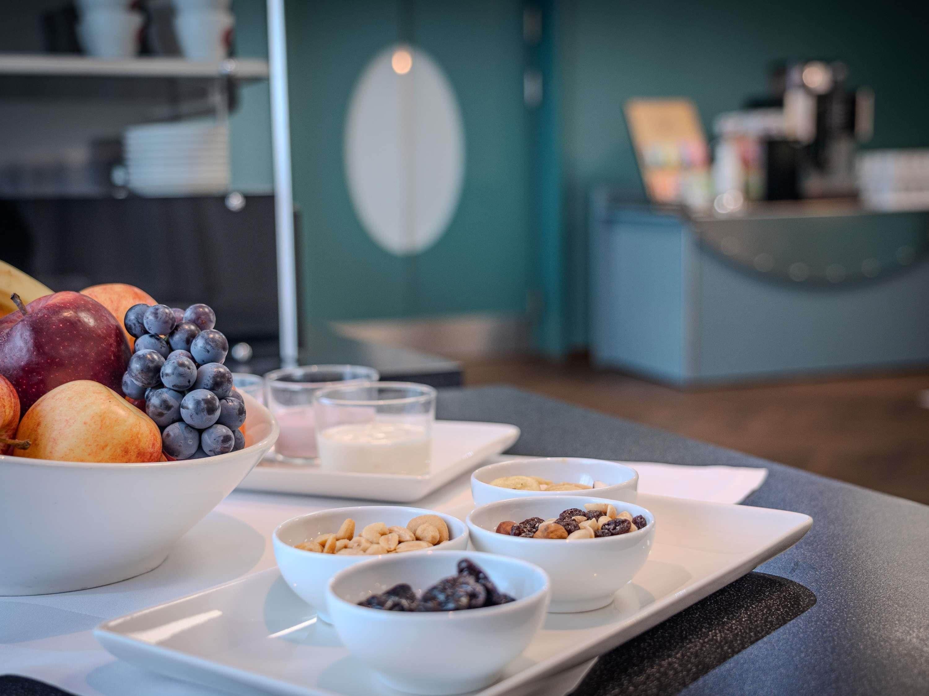 Un desayuno con frutas, nueces y una cafetera al fondo.