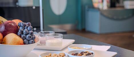 Un desayuno con frutas, nueces y una cafetera al fondo.