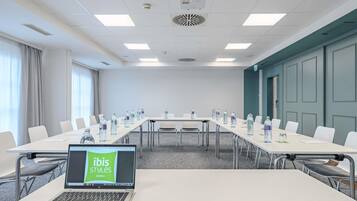 A conference room with a long table, chairs, a projector, and a laptop displaying 'ibis Styles Hotels'.