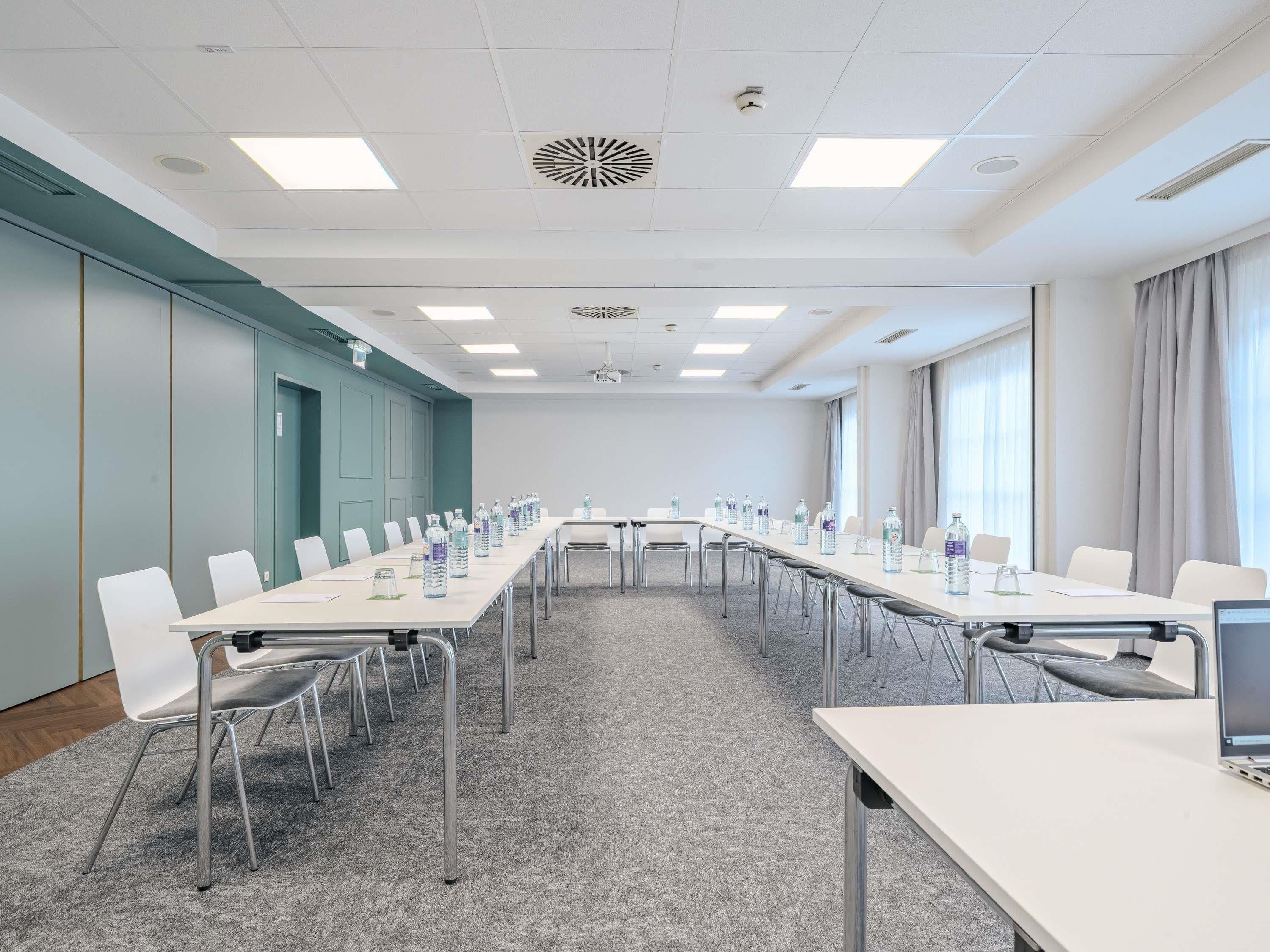 Ett konferensrum med långa bord, stolar, vattenflaskor och en projektorduk.
