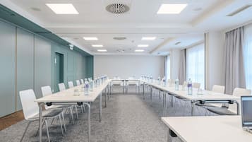 Une salle de conférence équipée de longues tables, de chaises, de bouteilles d’eau et d’un écran de projection.