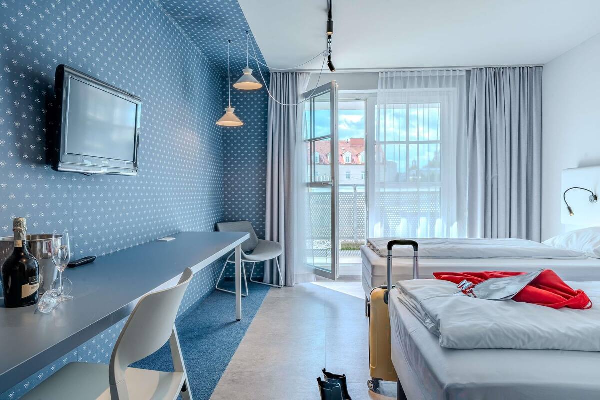 Quarto de hotel com cama, escrivaninha com cadeira, televisão e mala.