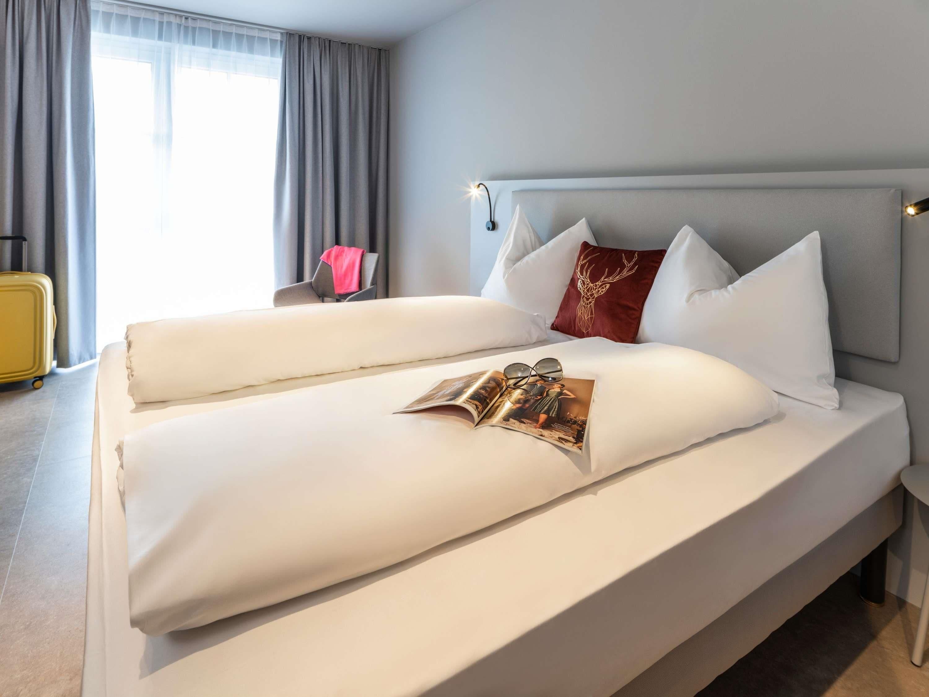 A neatly made bed with white linens and a magazine on it.