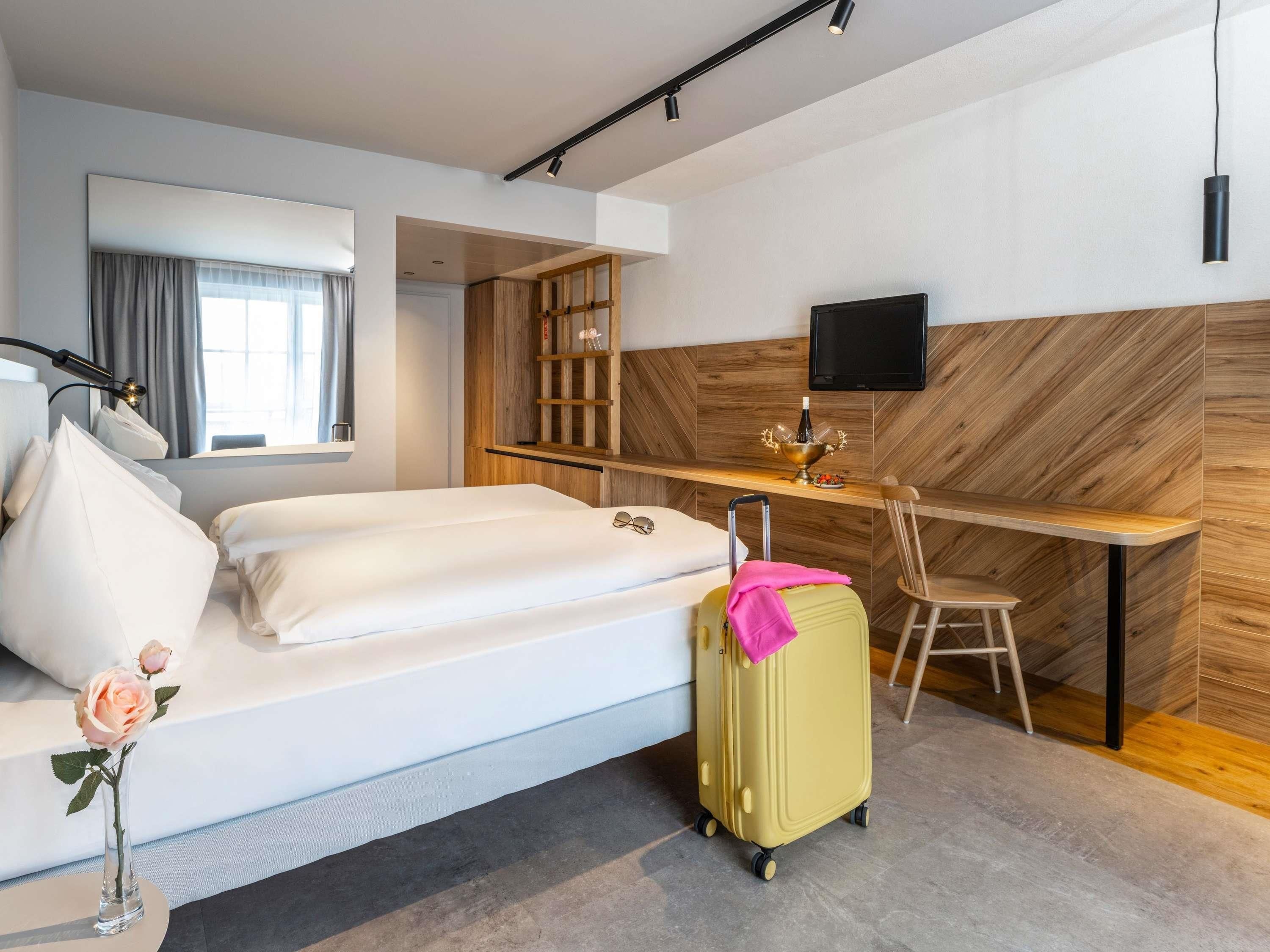 Una habitación de hotel con una cama, un escritorio, una silla, un televisor y una maleta.