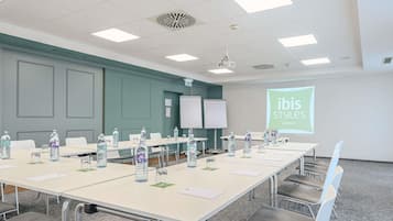 Ein Konferenzraum mit einem langen Tisch, Stühlen, Wasserflaschen und einer Projektionsleinwand, die 'ibis Styles Hotels' anzeigt.