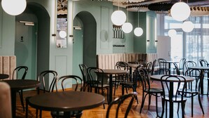 Interior de restaurante con mesas redondas, sillas negras y farolillos de papel colgantes.