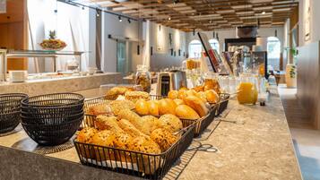 A breakfast buffet with various breads and pastries, a coffee station, and a juice bar.