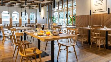 Un espace de restauration moderne avec des tables et des chaises en bois, de grandes fenêtres et une enseigne indiquant « STEIRERHUT ».