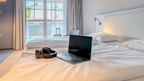 Une chambre d’hôtel avec un lit, un ordinateur portable et des écouteurs posés sur le lit.