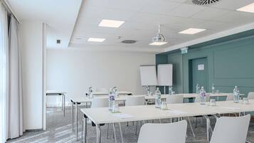 Un salón de conferencias con mesas, sillas, botellas de agua, una pizarra y un proyector.