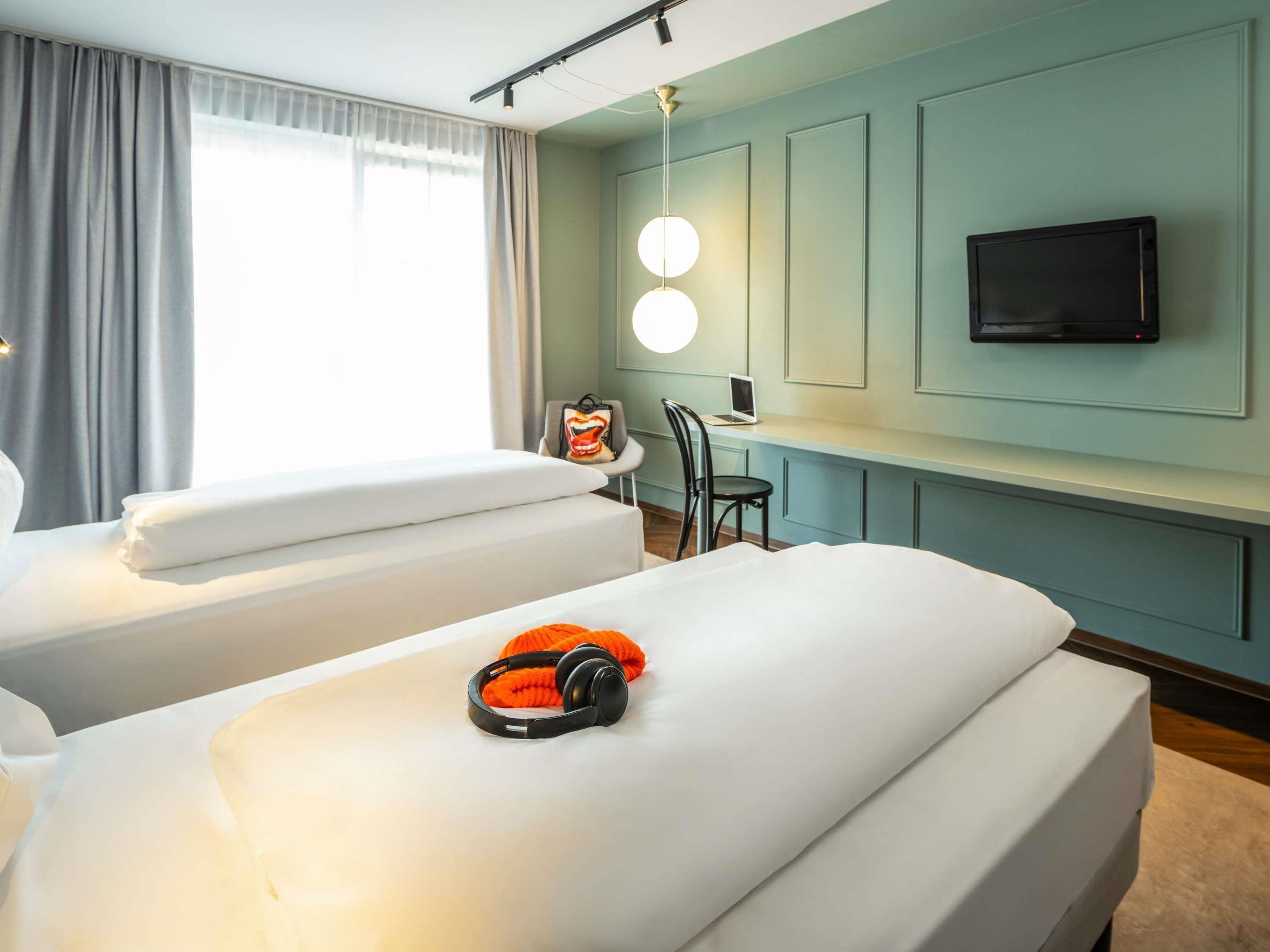 A hotel room with two beds, a desk with a laptop, a TV, and a window with curtains.