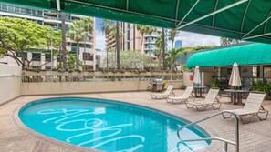 Relax by the pool surrounded by lounge chairs and a covered seating area, with a grill and potted plants nearby.