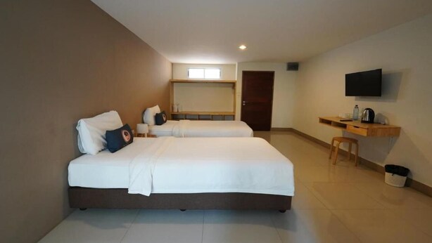 A hotel room with two beds, a desk with a chair, a TV mounted on the wall, and a small window. - RoomQuest Tha Sala (Chiang Mai)