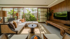 Ein modernes Wohnzimmer mit Sofa, Couchtisch und Fernseher, ausgestattet mit großen Fenstern und Zimmerpflanzen.