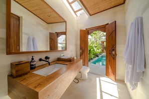Ein modernes Badezimmer mit einem Holzkosmetikschrank, einem großen Spiegel und Blick auf einen Pool durch eine offene Tür.