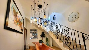 A staircase with a black wrought iron railing, a wooden bench, and a chandelier with multiple light bulbs. - Zland is your destination Vacation (San Juan)