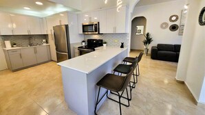 A modern kitchen with a central island, stainless steel appliances, and a seating area with a black sofa and chairs. - Zland is your destination Vacation (San Juan)