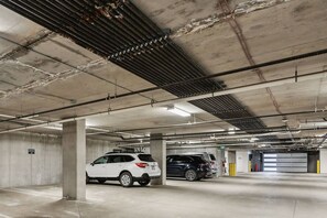 Eine mehrstöckige Parkgarage mit Betonpfeilern, Deckenbeleuchtung und zwei geparkten Autos.
