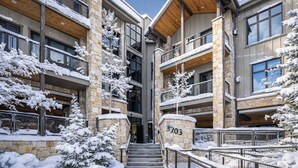Ein mehrstöckiges Gebäude mit Stein- und Holzfassade, schneebedeckte Bäume und einer Treppe, die zum Eingang führt.