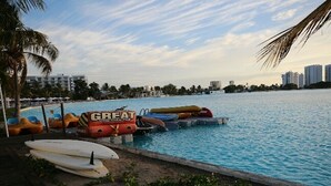 A pool area with inflatable water toys and surfboards, surrounded by palm trees and buildings in the background.