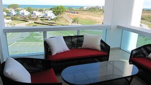 A balcony with wicker furniture, a glass table, and a view of a golf course and buildings.