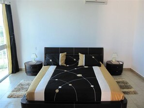 Un dormitorio con una colcha blanco y negro, dos mesitas de noche con lámparas y una ventana con cortinas.