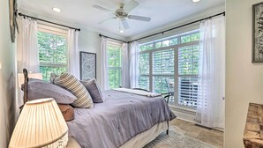 Un dormitorio con cama, ventilador de techo y ventanas grandes con contraventanas.