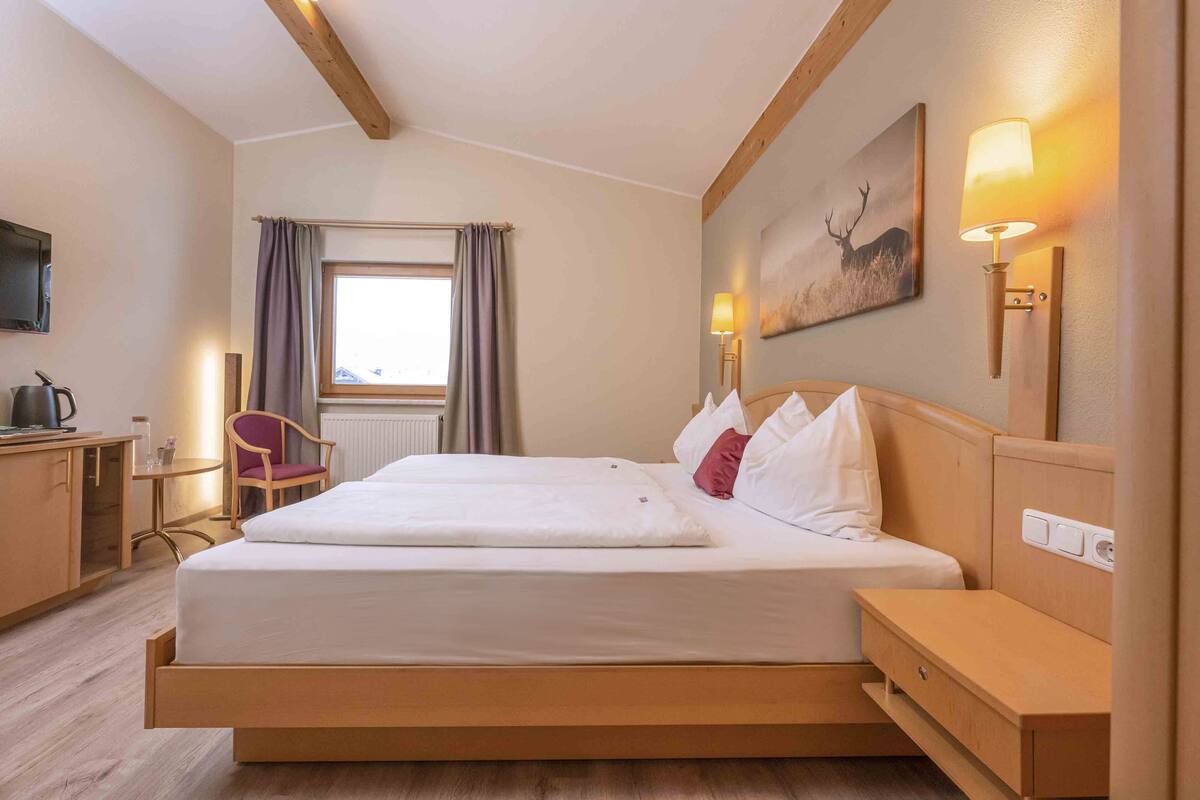 Et hotelværelse med seng, natbord, lampe, kunst og et vindue med gardiner.