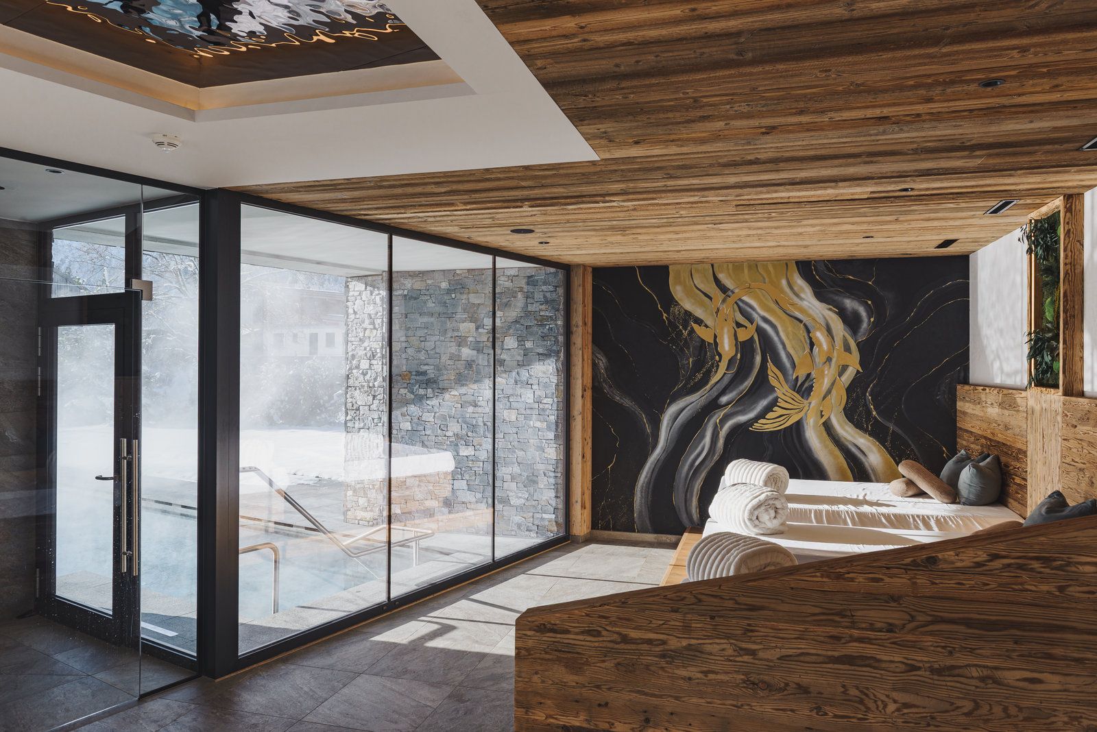 Ein modernes Interieur mit einer großen Glastür, die zu einem Außenbereich führt, einer Holzzieldecke und einer Marmorwand mit goldenem Dekor.