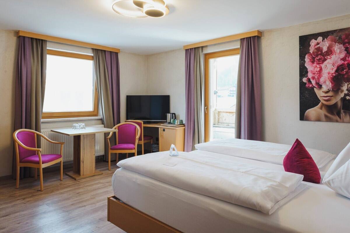 Et hotelværelse med en seng, to stole, et skrivebord, et fjernsyn og et billede på væggen.
