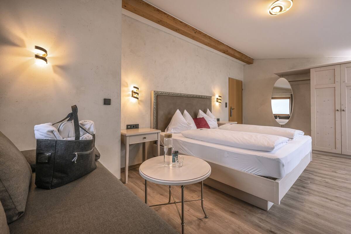 Et hotelværelse med en seng, sengeborde, et lille rundt bord, en sofa, en vægmonteret lampe og et spejl.