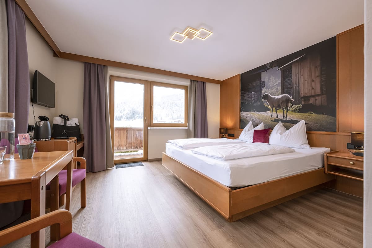 Et moderne hotelværelse med en stor seng, et skrivebord med stol, et fjernsyn og et maleri af en fåre på væggen.