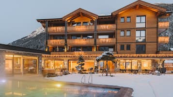 Ein mehrstöckiges Hotel mit Poolbereich, umgeben von schneebedeckten Bergen.