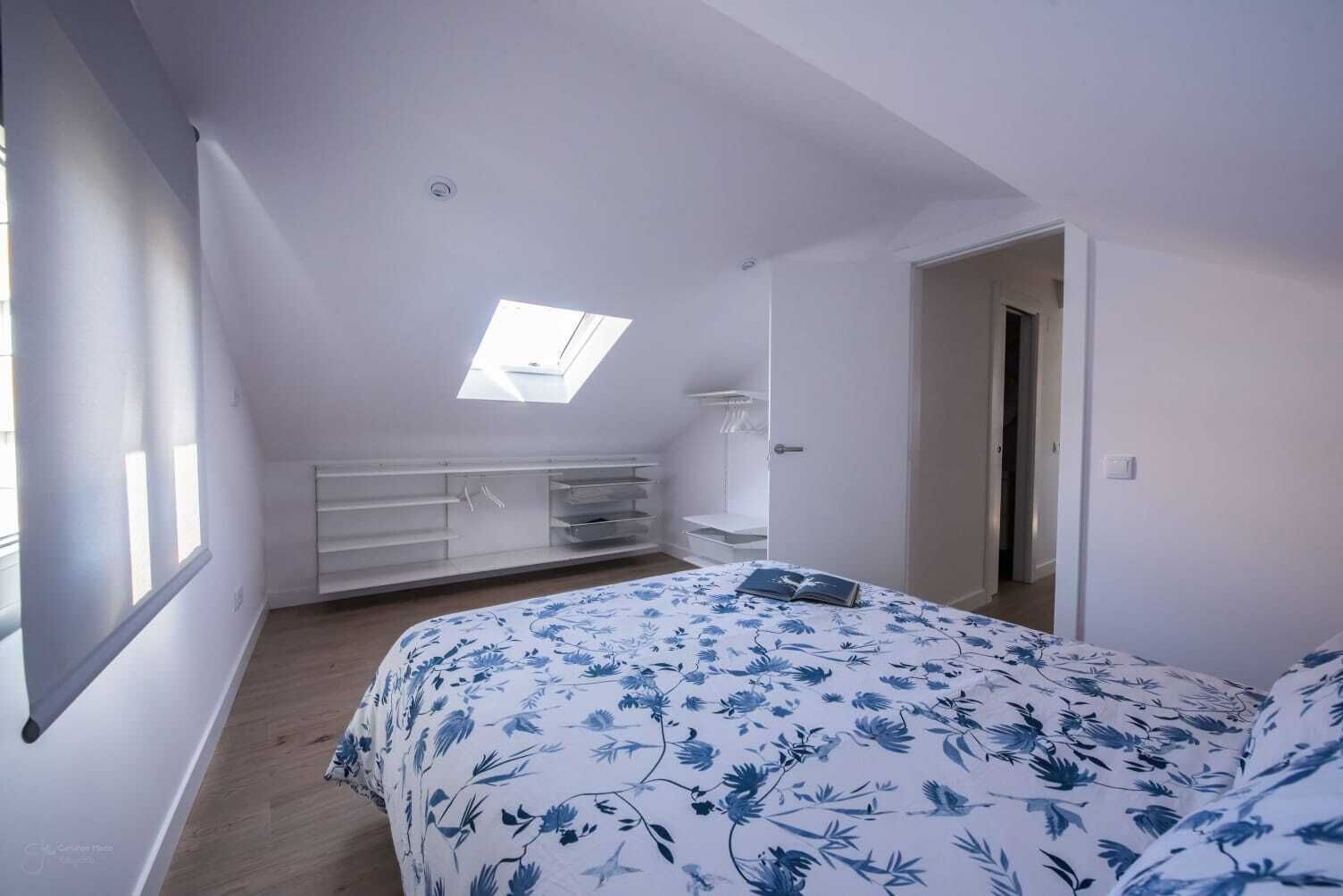 Een slaapkamer met dakraam, een bed met bloemenbedrukking, een kledingkast en een deur naar een andere kamer.