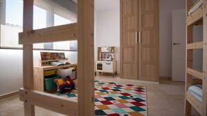Ein Kinderzimmer mit Etagenbetten, einem Schreibtisch, einem Kleiderschrank und einem bunten Teppich.
