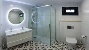 Ein modernes Badezimmer mit einer Duschkabine, einem Doppelwaschtisch, einer Toilette und einem kleinen Fenster.