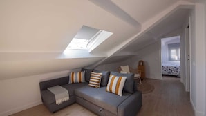 Ein modernes Schlafzimmer im Loftsstil mit schrägem Dach, einem grauen Modulsessel und einem kleinen Holzstuhl.