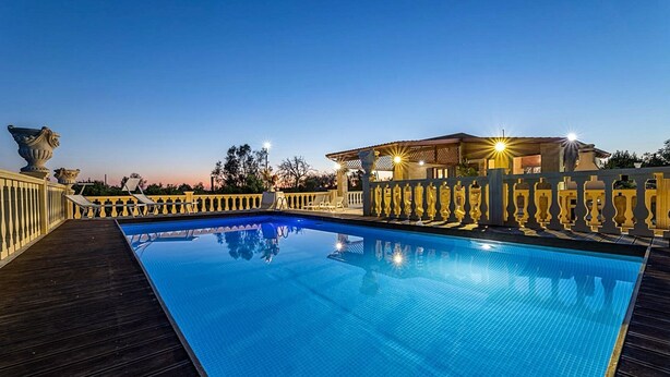 Une piscine avec une terrasse en bois et une pergola illuminée.