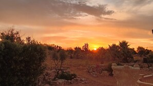 Une vue sur le coucher de soleil, avec un sentier en pierre menant à un bâtiment agrémenté d’une urne décorative.