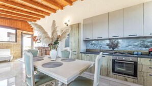 Une cuisine moderne avec des meubles blancs, un îlot central doté de chaises et un pare-feu en pierre.