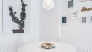 Zona de menjador moderna amb una taula rodona blanca, cadires blanques, una làmpada penjant i una paret amb quadres i un cartell decoratiu.