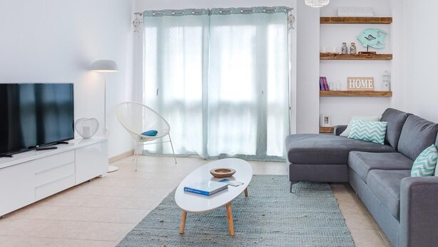 Un saló modern amb televisió de pantalla plana, una taula de cafè blanca, un sofà gris i una catifa blava.