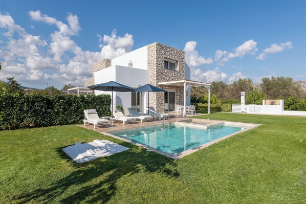 A modern house with a swimming pool, outdoor seating, and a stone facade.