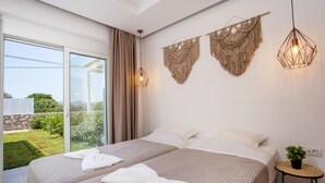 Een slaapkamer met twee bedden, een grote schuifdeur naar een balkon, macramé wanddecoraties en een klein rond tafeltje met een plant.