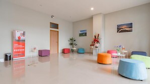 A modern hotel lobby with a clean, minimalist design, featuring a reception desk, colorful seating areas, and a large window with a scenic view. - Sans Stay Karapitan Street (Bandung)