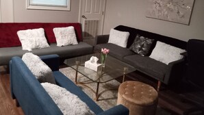 A living room with a grey sofa, blue sofa, and ottoman, a glass coffee table, and a red throw blanket. - Luxury Cherry Blossom Suite 15 min from Downtown (Washington)
