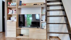 A modern room with a built-in TV, wooden flooring, and a staircase. - Cute Compact One BHK Apartment Near Center ! 10 mins walk (Cluj-Napoca)