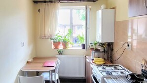 A compact kitchen with a dining table, chairs, a stove, and a window with potted plants. - Cute Compact One BHK Apartment Near Center ! 10 mins walk (Cluj-Napoca)