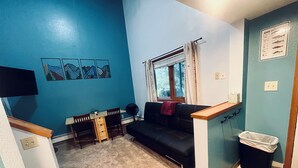 A small living room with a blue wall, a black sofa, a wooden table, and a window with curtains. - Valdez Robe River Front Property (Valdez)